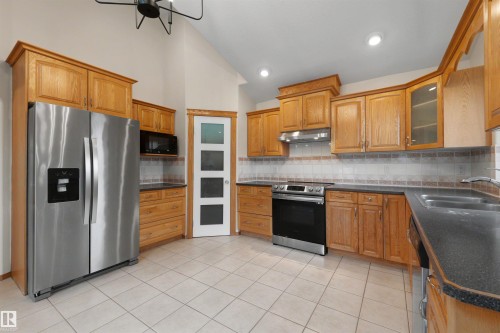 Kitchen featuring light wood cabinetry, stainless steel appliances, dark countertops, a tiled backsplash, and light tile flooring - 15227 47 Street, Edmonton, AB 