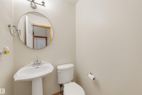 Pedestal sink with chrome faucet, round wall mirror, and overhead vanity lighting - 15227 47 Street, Edmonton, AB 