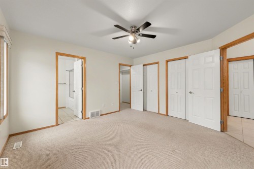 Carpeted room featuring a ceiling fan with integrated lighting, multiple white panel doors, wood-trim doorways, and a window with blinds - 15227 47 Street, Edmonton, AB 