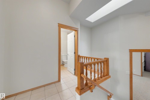 Upper landing featuring a natural wood handrail and balusters, a skylight, and light neutral wall paint - 15227 47 Street, Edmonton, AB 