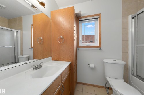Bathroom featuring a single-sink vanity with white countertop, wood-finish cabinetry, built-in storage, a sliding glass shower, and a framed window - 15227 47 Street, Edmonton, AB 