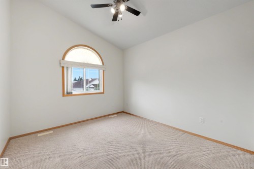 Vaulted ceiling room featuring a large arched window with wood-finish trim, neutral carpet, and a ceiling fan with integrated lighting - 15227 47 Street, Edmonton, AB 