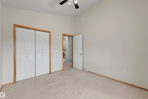 Carpeted room featuring a ceiling fan, light-toned walls, and wood-finish trim - 15227 47 Street, Edmonton, AB 