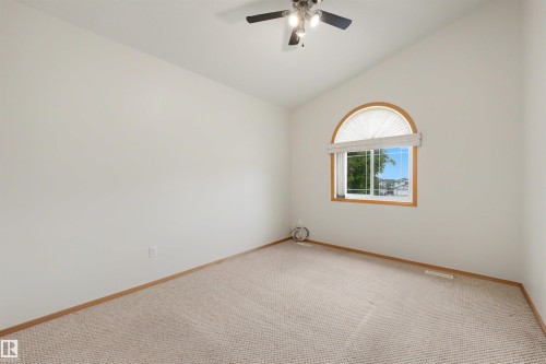 Room featuring vaulted ceilings, neutral carpeting, and an arched window with wood-finish trim - 15227 47 Street, Edmonton, AB 