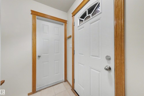 Entryway featuring a paneled door with an arched transom window, a secondary paneled door, light-toned wall paint, decorative wood trim, and square floor tiles - 15227 47 Street, Edmonton, AB 