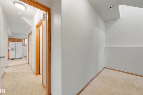 Hallway with wood-finish door frames, light neutral wall paint, and square tile flooring - 15227 47 Street, Edmonton, AB 