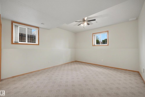 Spacious room featuring patterned carpeting, light-toned walls with wainscoting, and wood-trimmed windows providing natural light - 15227 47 Street, Edmonton, AB 