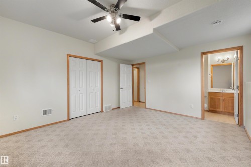 Spacious room featuring patterned carpet flooring, bi-fold closet doors, a ceiling fan with integrated lighting, and an entryway to a bathroom with a vanity and mirror - 15227 47 Street, Edmonton, AB 