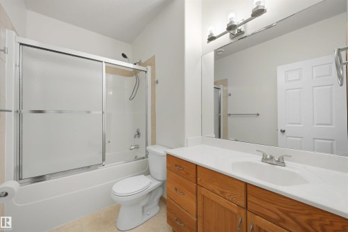 Full bathroom featuring a tub and shower combination with sliding glass doors, a vanity with wood-finish cabinetry, a white countertop, and a large mirror - 15227 47 Street, Edmonton, AB 