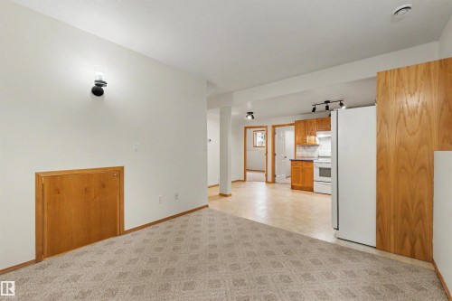 Carpeted living area featuring a wall sconce, wood paneling, and a wood-finish baseboard - 15227 47 Street, Edmonton, AB 