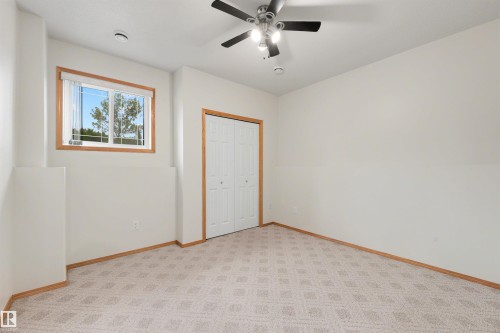 Room featuring light-toned patterned carpet, a ceiling fan with integrated lighting, and a window with wood-trim framing - 15227 47 Street, Edmonton, AB 