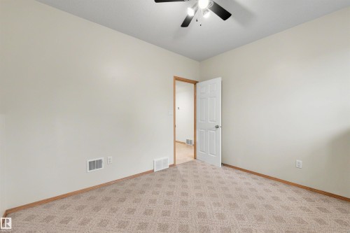 Interior room featuring neutral wall paint, patterned carpet flooring, a white paneled door, and a ceiling fan with integrated lighting - 15227 47 Street, Edmonton, AB 