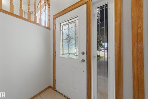 Entryway featuring a white door with decorative glass insert, a full-length sidelight, and wood-finish trim - 15227 47 Street, Edmonton, AB 