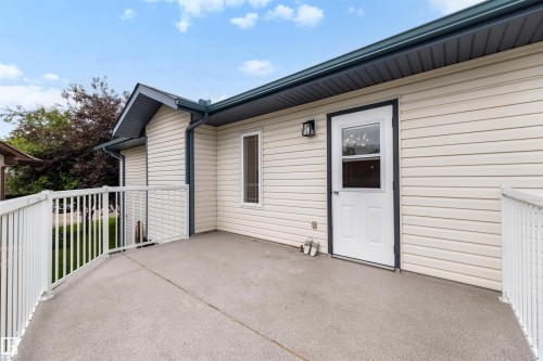 Spacious outdoor deck featuring light-colored siding, a white metal railing, and a glass-paneled exterior door - 15227 47 Street, Edmonton, AB 