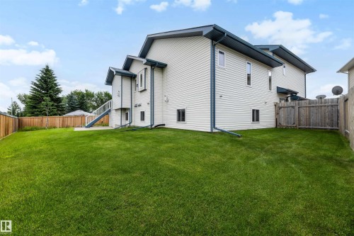 Expansive backyard featuring a lush lawn, wooden privacy fencing, and mature evergreen trees - 15227 47 Street, Edmonton, AB 