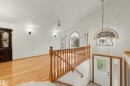 Two-story foyer featuring a prominent staircase with wood banister, a decorative entry door with leaded glass, and a contemporary black metal chandelier - 15227 47 Street, Edmonton, AB 