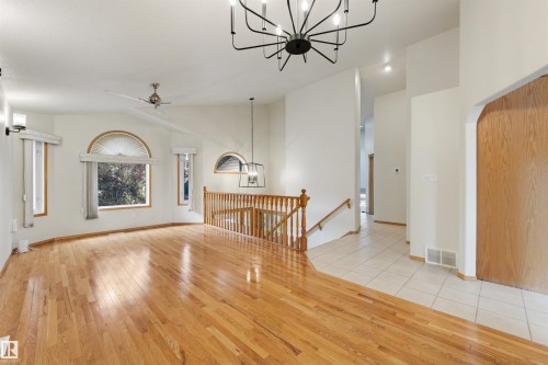 Hardwood flooring and tile entry, vaulted ceiling with contemporary chandelier, arched and rectangular windows, and a wood spindle railing - 15227 47 Street, Edmonton, AB 