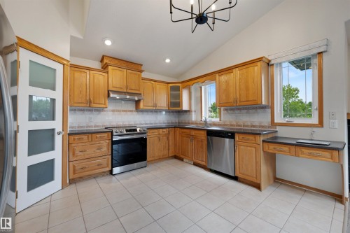 Kitchen featuring natural wood cabinetry, dark countertops, a tiled backsplash, and stainless steel appliances - 15227 47 Street, Edmonton, AB 
