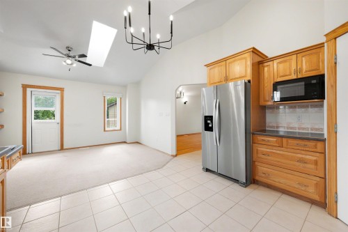 Kitchen and living area featuring a vaulted ceiling with skylight, tile flooring, stainless steel refrigerator, built-in microwave, and wood cabinetry - 15227 47 Street, Edmonton, AB 