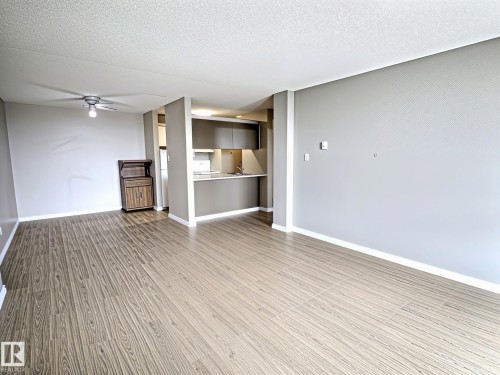 Open-concept living area featuring wood-finish flooring, a contemporary ceiling fan, and a kitchen pass-through with a breakfast bar - 1105 11007 83 Avenue, Edmonton, AB 
