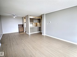 Open-concept living area featuring wood-finish flooring, a contemporary ceiling fan, and a kitchen pass-through with a breakfast bar - 
