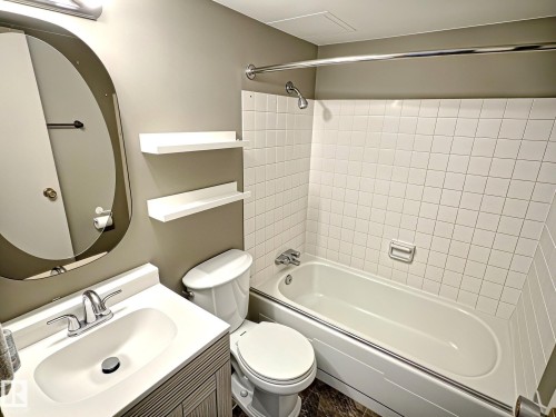Full bathroom featuring a white vanity with integrated sink, chrome faucet, oval mirror, and a full-size bathtub with white subway tile surround - 1105 11007 83 Avenue, Edmonton, AB 