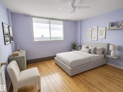 Spacious bedroom featuring wide plank wood-finish flooring, a large sliding window, a ceiling fan, and light purple wall tones - 