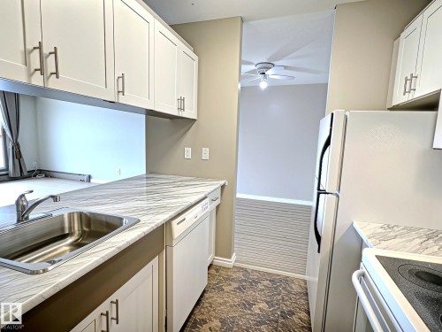 Kitchen featuring white shaker-style cabinetry with brushed nickel hardware, a stainless steel sink, and white-marbled countertops - 1105 11007 83 Avenue, Edmonton, AB 