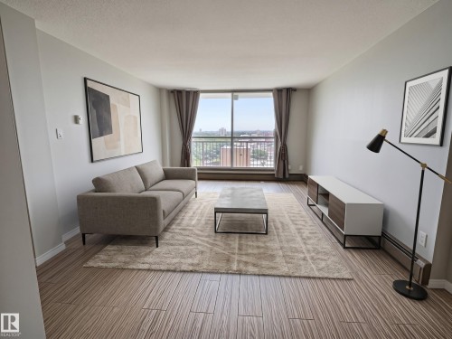 Spacious living area featuring expansive windows, wood-finish flooring, and white baseboards - 1105 11007 83 Avenue, Edmonton, AB 