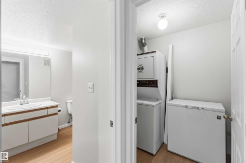 Dedicated laundry area featuring a stacked washer and dryer, accompanied by a chest freezer - #304 4924 19 Av Nw, Edmonton, AB 