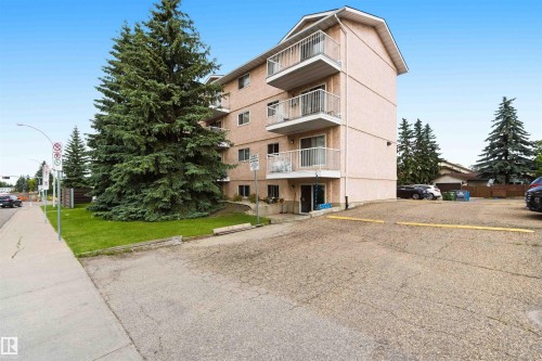 Multi-story building featuring light-colored stucco exterior, multiple balconies with white railings, and an adjacent paved parking area - #304 4924 19 Av Nw, Edmonton, AB 