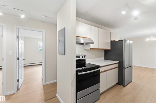 Kitchen featuring white cabinetry, light wood-finish flooring, a stainless steel range hood, and a stainless steel refrigerator - #304 4924 19 Av Nw, Edmonton, AB 