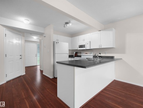 Open-concept kitchen featuring white cabinetry, dark countertops, and integrated appliances - 16106 131A Street, Edmonton, AB 