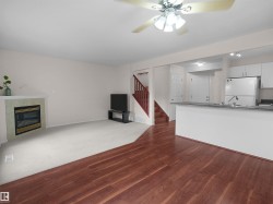 Open-concept living area featuring a fireplace with a tile surround and white mantel, wood-finish flooring, and a ceiling fan with integrated lighting - 