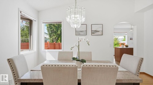 Vaulted ceilings illuminate the dining area, featuring a modern chandelier, two windows, and an arched doorway - 1225 Kane Wynd, Edmonton, AB 