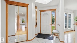 Entryway featuring white tile flooring, natural wood trim, a skylight, a white paneled front door with a transom window, and a mirrored closet with wood trim - 