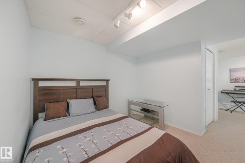 Wood-finish headboard, light-colored walls, recessed ceiling panel, and track lighting - 1225 Kane Wynd Nw, Edmonton, AB - Indoor Photo Showing Bedroom