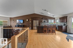 Open-concept kitchen and living area featuring light wood-finish flooring, dark wood cabinetry, a central island with countertop seating, and a decorative tile backsplash - 