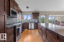 Kitchen featuring dark wood cabinetry, stainless steel appliances, mosaic tile backsplash, and light wood-finish flooring - 