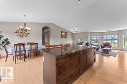 Open-concept living area featuring a kitchen island with dark cabinetry and a speckled countertop, a dining area with a chandelier, and a living space with multiple windows - 