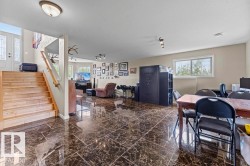 Spacious lower-level area featuring polished dark marble-look tile flooring, natural wood stairs, and a bright window - 