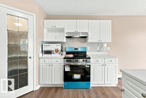 Kitchen featuring white shaker-style cabinetry, a built-in range hood, white countertops, and a full-height backsplash with a marble-effect pattern - 2811 33 Street, Edmonton, AB 