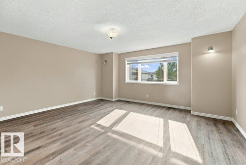 Spacious interior room featuring wood-finish flooring, a neutral wall palette, and a large multi-pane window - 2811 33 Street, Edmonton, AB 