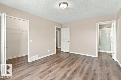 Spacious room featuring wood-finish flooring, neutral-toned walls, a built-in closet with wire shelving, and an en-suite bathroom with a glass-enclosed shower - 2811 33 Street, Edmonton, AB 