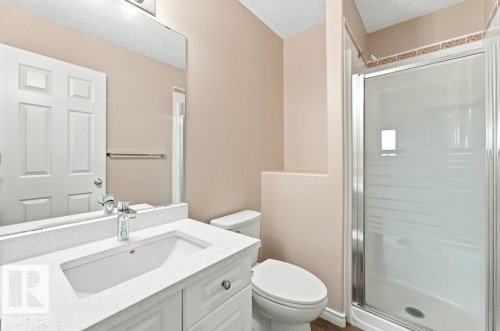 Bathroom featuring a white vanity with an integrated sink and chrome faucet, a large frameless mirror, and a glass-enclosed shower with a tiled accent band - 2811 33 Street, Edmonton, AB 