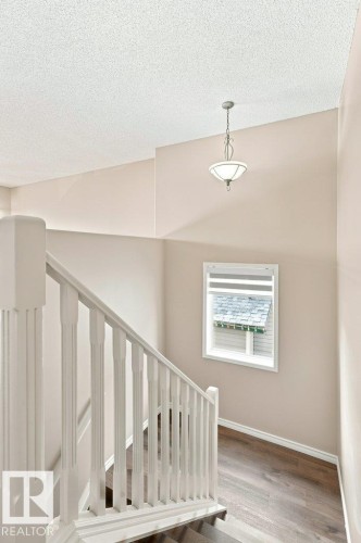 Staircase featuring white balusters and newel posts, wood-finish flooring, a window with horizontal blinds, and a suspended ceiling light fixture - 2811 33 Street, Edmonton, AB 