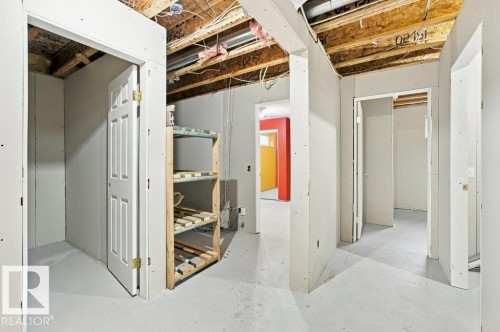 Unfinished basement space with exposed ceiling joists and wiring, featuring partial drywall installation, multiple open doorways, and a concrete floor - 2811 33 Street, Edmonton, AB 