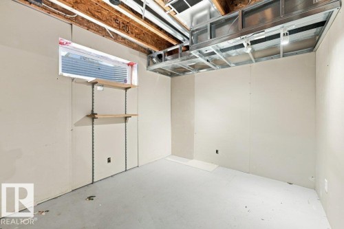 Unfinished basement room featuring exposed ceiling joists, metal ductwork, and an egress window with a window well - 2811 33 Street, Edmonton, AB 