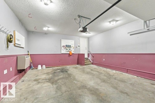Spacious garage featuring a concrete floor, built-in overhead lighting, and interior access via a white door and small staircase - 2811 33 Street, Edmonton, AB 