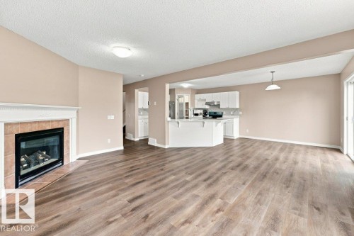 Spacious living area featuring wood-finish flooring, a tiled fireplace with a white mantel, and neutral wall tones - 2811 33 Street, Edmonton, AB 